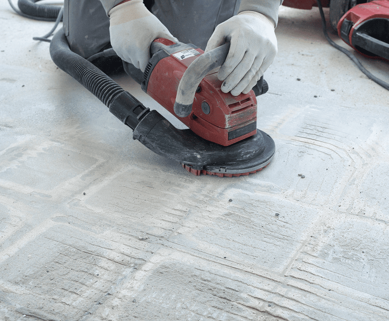 Worker using floor sander on concrete surface.