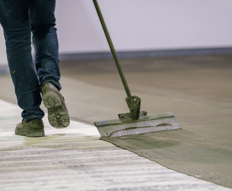 Worker smoothing concrete floor with tool.