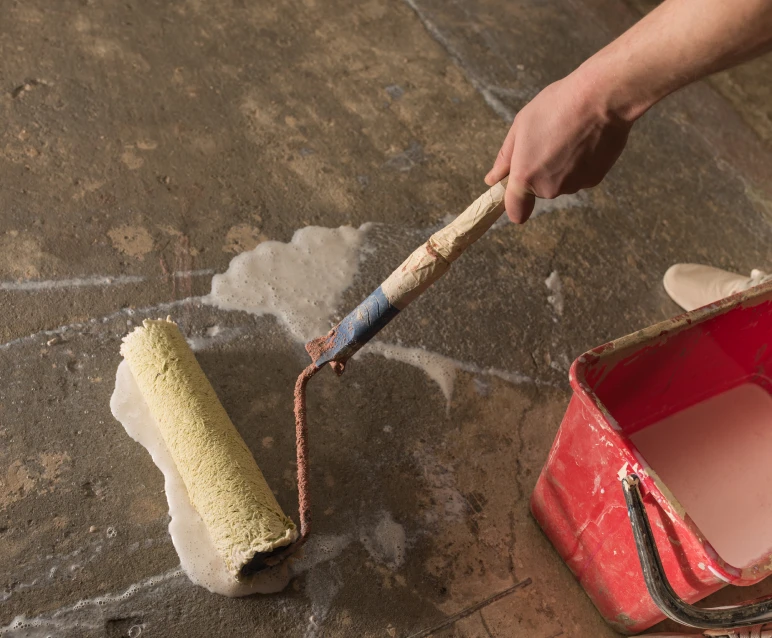 Hand using roller to paint concrete floor.